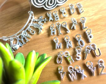 May include: A set of silver charm letters, A through Z, with a silver bangle bracelet. The charms are small and delicate, perfect for adding a personalised touch to any jewellery collection.