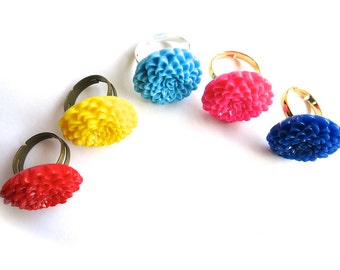 Op de afbeelding: Een verzameling verstelbare ringen met bloemvormige ontwerpen in verschillende kleuren. De ringen tonen heldere tinten rood, geel, roze, blauw en lichtblauw. De bloemelementen staan centraal, tegen een witte achtergrond.