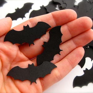 K&ouml;nnte beinhalten: Eine Hand h&auml;lt eine Handvoll schwarzer Fledermaus-Ausschnitte aus Papier. Die Flederm&auml;use sind in verschiedenen Gr&ouml;&szlig;en und Formen.