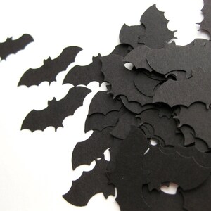 K&ouml;nnte beinhalten: Schwarze Papierflederm&auml;use, die auf einem wei&szlig;en Hintergrund verstreut sind. Die Flederm&auml;use sind in verschiedenen Gr&ouml;&szlig;en und Positionen angeordnet und schaffen eine festliche Halloween-Atmosph&auml;re.