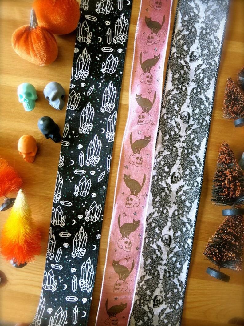 Puede incluir: Tres cintas diferentes con tem&aacute;tica de Halloween. La primera cinta es negra con dise&ntilde;os de cristales blancos y calaveras. La segunda cinta es rosa con gatos negros y calaveras. La tercera cinta es blanca con encaje negro y dise&ntilde;os de calaveras.