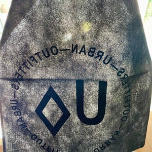May include: Black reusable tote bag with the text "Urban Outfitters" printed in a circle around a diamond and the letter "U".