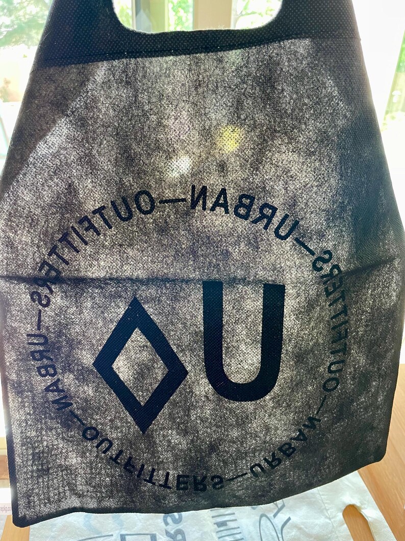May include: Black reusable tote bag with the text "Urban Outfitters" printed in a circle around a diamond and the letter "U".