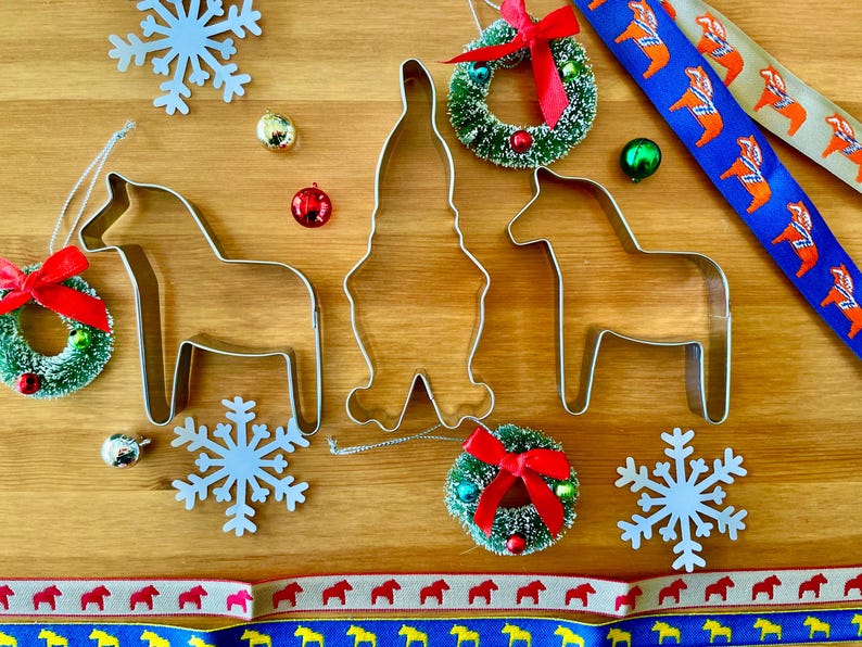 Puede incluir: Decoraciones navide&ntilde;as sobre una superficie de madera. La imagen incluye cortadores de galletas de metal con forma de caballo y gnomo, peque&ntilde;as coronas con lazos rojos, adornos de copos de nieve y cintas decorativas con motivos de caballos.