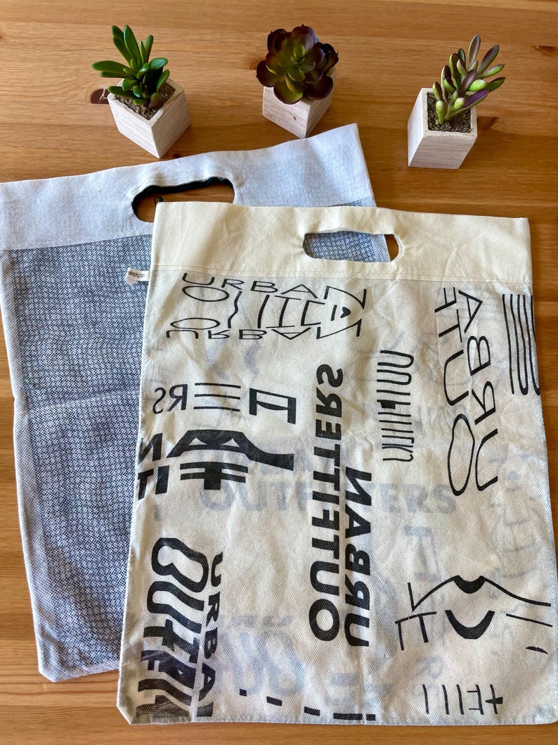 May include: Two reusable shopping bags. One is blue with a white pattern and the other is beige with black text that says "Urban Outfitters".