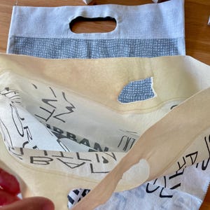 May include: A white canvas tote bag with black text that reads "URBAN" and "CITY" on the front. The bag is folded in half, revealing a blue and white patterned lining.