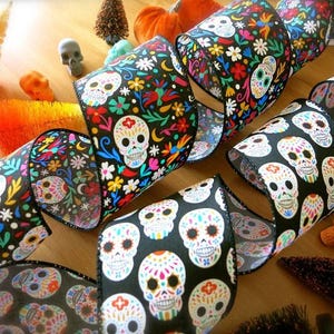 Puede incluir: Cinta negra y blanca con un patr&oacute;n de calavera de az&uacute;car colorido. La cinta est&aacute; decorada con flores y espirales.