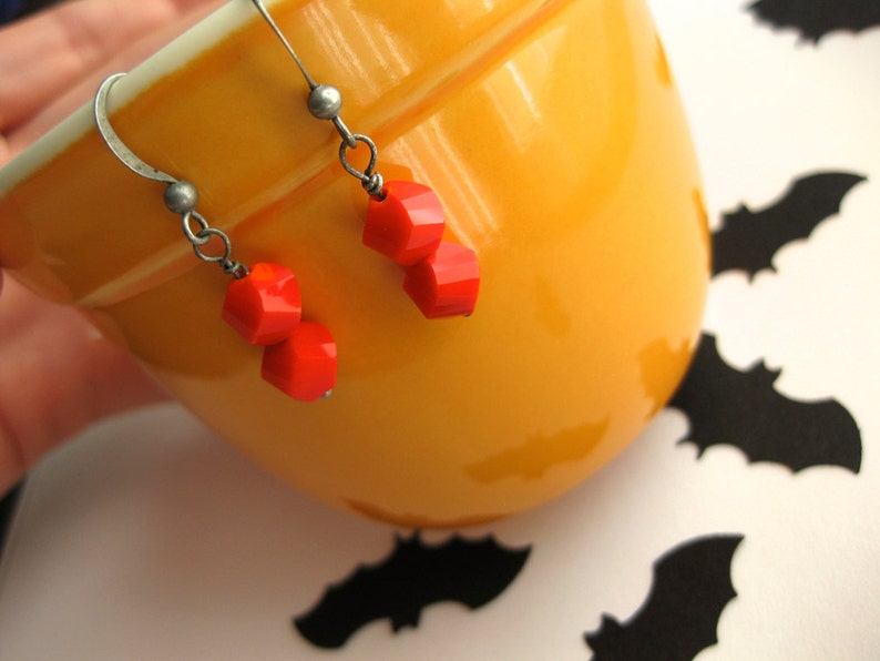 K&ouml;nnte beinhalten: Ein Paar Ohrringe mit orangefarbenen Glasperlen, die an silbernen Haken h&auml;ngen. Die Ohrringe werden auf einer gelben Keramikschale pr&auml;sentiert.