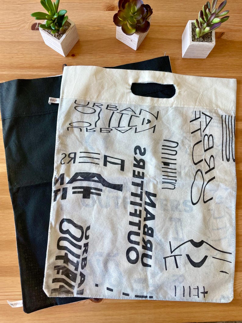 May include: Two reusable shopping bags. One is black and the other is white with a black print of the words "Urban Outfitters" repeated in different sizes and orientations.