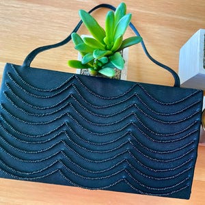 May include: A black satin evening bag with a beaded wave pattern. The bag has a long strap and is closed with a magnetic clasp.
