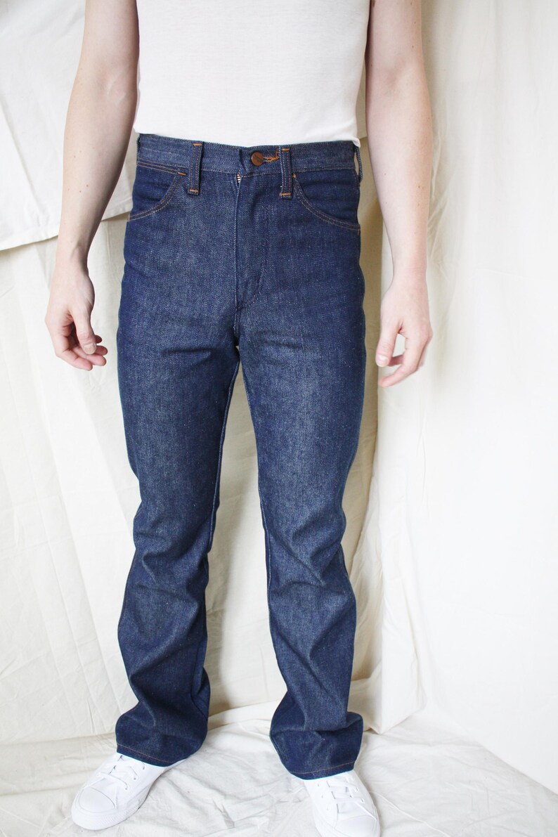 May include: Dark blue denim jeans with a classic five-pocket design. The jeans have a button and zipper closure, and a straight leg fit. The model is wearing a white t-shirt and white sneakers.