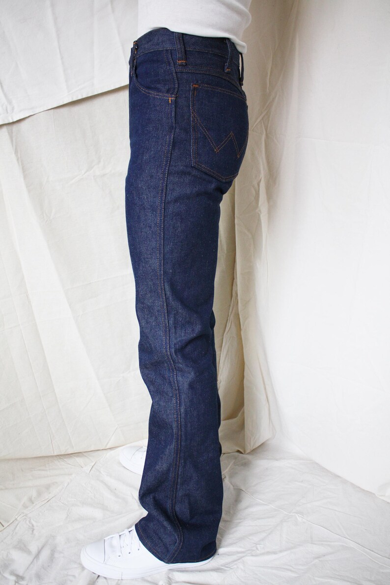 May include: Dark blue denim jeans with a classic five-pocket design. The jeans have a straight leg fit and are worn with white sneakers. The back pocket features a distinctive stitching pattern. The jeans are made of a sturdy denim material.