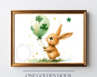 May include: Watercolor illustration of a brown bunny holding a green balloon decorated with shamrocks. The bunny stands on green grass, with gold stars scattered around. The artwork is framed in a gold frame. Text at the bottom reads "ONE GOLDEN HOUR GALLERY".