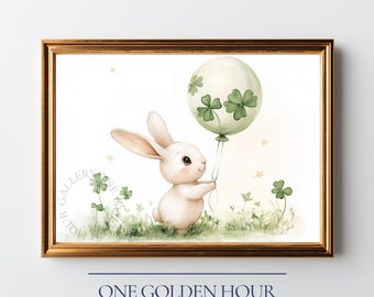 May include: A framed watercolor print featuring a white bunny holding a green balloon decorated with shamrocks. The bunny stands in a field of green grass and clovers. The print is in a gold frame with the text "ONE GOLDEN HOUR GALLERY".
