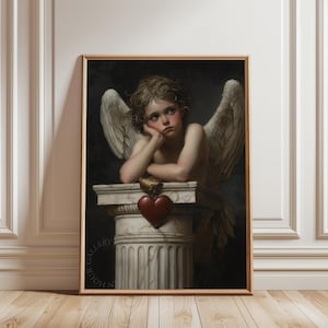 May include: A framed print of a classical painting featuring a cherubic angel with wings, resting its head on its hand. A red heart hangs from a stone pillar. The artwork has a dark background and is in a gold frame.