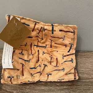 May include: A beige quilted pot holder with a pattern of various hammers and tools. The text "CARE INSTRUCTIONS" is printed on a tag attached to the pot holder.
