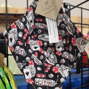 May include: A black and white bowl cozy with a casino-themed pattern. The design includes playing cards, dice, and poker chips in red and white. A tag with instructions is attached.