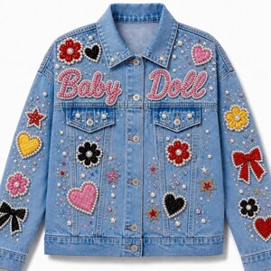 May include: A light blue denim jacket featuring the text Baby Doll in pink beaded lettering across the chest. The jacket is decorated with various patches including flowers, hearts, stars, and bows, all accented with white pearls and small crystals.