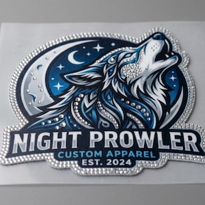Può includere: Toppa tempestata di strass con un lupo che ulula. Il lupo è ambientato su un cielo notturno blu scuro con una luna crescente e stelle. Il testo "NIGHT PROWLER CUSTOM APPAREL EST. 2024" è visualizzato sotto.