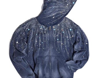 May include: A dark blue, acid-washed zip-up hoodie featuring a hood and long sleeves. The garment is decorated with a dense pattern of small, shimmering silver rhinestones that cascade downwards from the shoulders and across the hood.
