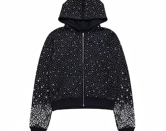 May include: Black zip-up hoodie covered in white, sparkling embellishments. The hoodie features a drawstring hood, a full-length zipper, and ribbed cuffs and hem. The embellishments are densely clustered, creating a starry night effect.