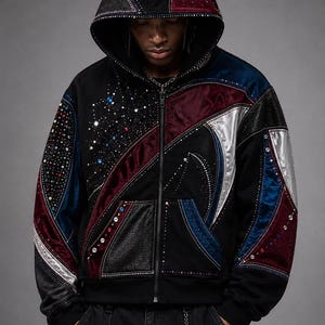 May include: A black zip-up hoodie featuring a complex patchwork design with panels of burgundy, blue, and silver fabric. The garment is heavily embellished with scattered rhinestones and studs across the hood, sleeves, and front panels.