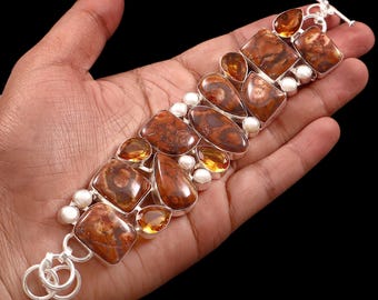 May include: A silver bracelet featuring a series of brown and orange patterned stones in various shapes, interspersed with small white pearls and amber-colored gems. The bracelet has a toggle clasp.