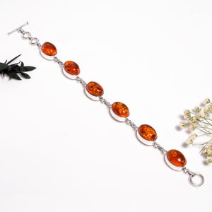 May include: A silver bracelet with oval amber stones. The amber stones are a warm, translucent orange colour, set in silver bezels. The bracelet has a toggle clasp and is displayed on a white surface.