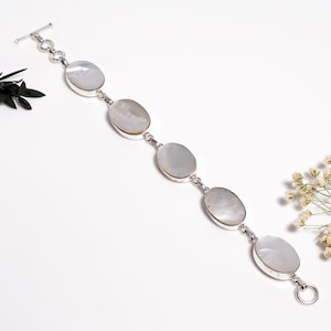 Può includere: Un bracciale in argento con cinque pietre ovali di madreperla iridescente. Le pietre sono collegate da maglie d'argento e incastonate in castoni d'argento. Il bracciale ha una chiusura a toggle.