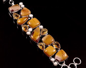 May include: A silver bracelet featuring a variety of polished gemstones in shades of brown, yellow, and cream. The bracelet includes square, teardrop, and oval-shaped stones, along with small, round pearls. The clasp is a toggle style.