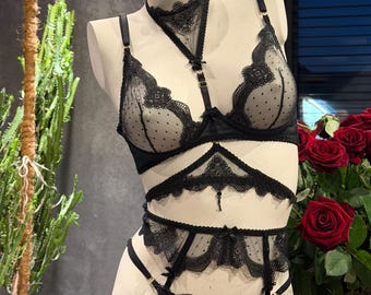 Peut inclure: Un ensemble de lingerie noir composé d'un soutien-gorge en maille transparente à pois avec bordure en dentelle, d'un tour de cou assorti avec anneau central, d'une pièce de taille en dentelle et d'un porte-jarretelles sur un mannequin.