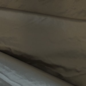 May include: Close-up of a dark gray fabric with a subtle sheen. The material is folded, creating shadows and highlights that emphasize its texture and drape. The fabric appears smooth and possibly lightweight.