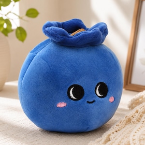 Könnte beinhalten: Ein blaues Plüsch-Blaubeerspielzeug mit einem lächelnden Gesicht, schwarzen Augen und rosa Wangen. Die Oberseite der Blaubeere hat ein dunkelblaues, blütenförmiges Design. Ein bezauberndes Kinderspielzeug, ca. 15 cm im Durchmesser.