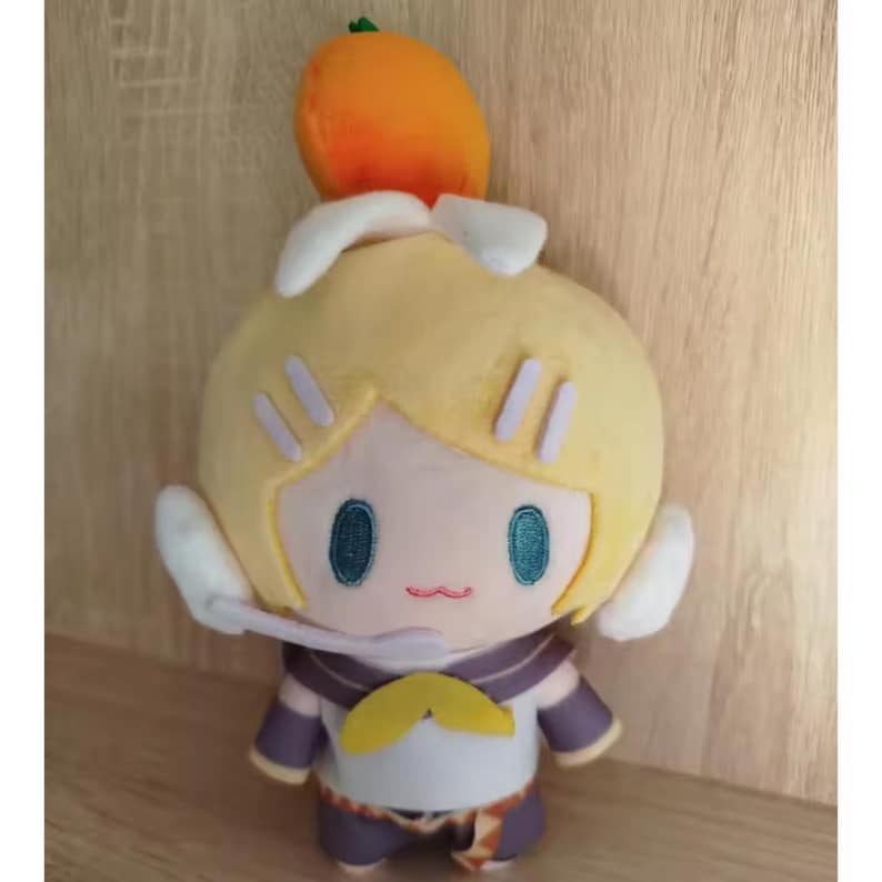 May include: A plush doll with a yellow head, blue eyes, and a small orange fruit on top. The doll has a white and purple outfit with a yellow bow. The doll is a cartoon character.
