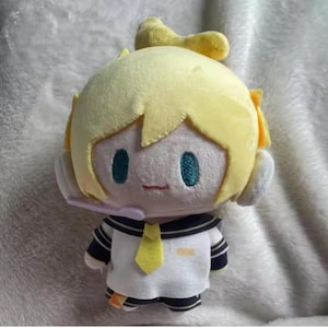 May include: A plush doll featuring a character with yellow hair, teal eyes, and a small red mouth. The doll wears a white sailor-style uniform with navy blue accents and a yellow tie. A headset is attached to the doll's head.