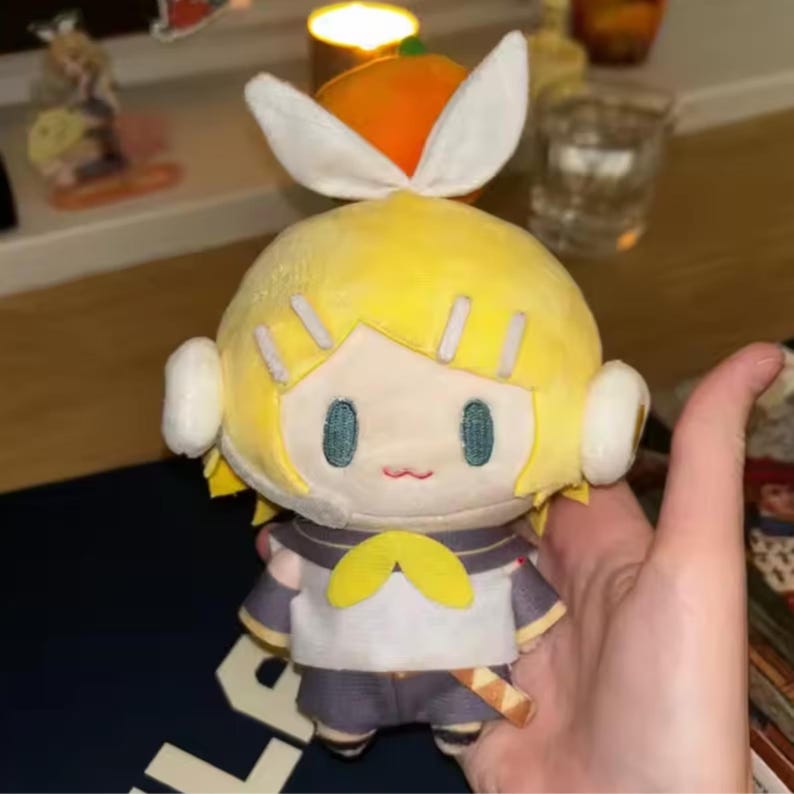 May include: A plush doll with yellow hair, blue eyes, and a small red mouth. The doll has a white and yellow outfit with a bow tie. The doll is holding a small wooden sword. The doll has white ear-like accessories and a white bow on top of its head.