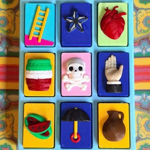 May include: A collection of nine colorful, rectangular decorative tiles. Each tile features a unique 3D design, including a ladder, star, heart, skull, hand, watermelon, umbrella, and a jug. The tiles are arranged in a light blue tray.