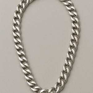 Könnte beinhalten: Eine silberfarbene Halskette mit großen, ineinandergreifenden Gliedern. Die Halskette hat einen sicheren Verschluss und wird vor einem neutralen, grauen Hintergrund präsentiert. Dieses Schmuckstück ist ein auffälliges Modeaccessoire.