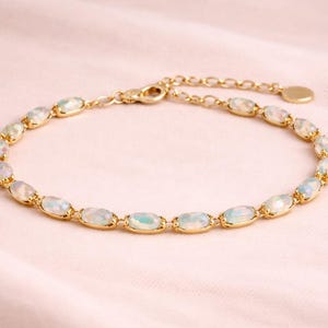 May include: A gold bracelet with oval opals. The opals are set in individual gold bezels and linked together. The bracelet is displayed on a pink fabric background. The bracelet's length is adjustable.