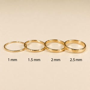 May include: Four gold rings with a hammered texture arranged in a row. The rings are labelled with their respective widths of 1 mm, 1.5 mm, 2 mm, and 2.5 mm, indicating the thickness of each band as shown in the text below each individual ring.