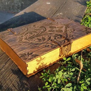 以下が含まれることがあります： 蓋に複雑な花の彫刻が施された、手作りの木製ボックス。ボックスは温かみのある茶色に着色され、エッジは明るい木材です。金属製の留め金とヒンジが付いており、ヴィンテージまたはアンティークスタイルを連想させます。