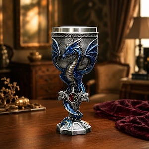 May include: A decorative goblet featuring a detailed blue dragon sculpture wrapped around the stem and bowl. The cup has a metallic silver finish with intricate textures, a smooth stainless steel rim, and a central red gemstone accent on the base.