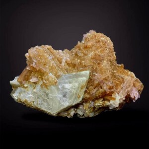 May include: A natural mineral specimen featuring a cluster of golden-brown crystals atop a pale, crystalline base. The crystals have a rough, textured appearance, with variations in color and form. The background is a solid black.