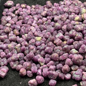 Puede incluir: Primer plano de un montón de piedras preciosas de rubí en bruto sin cortar. Las piedras son de un color rojo rosado intenso, con algunas zonas de rosa y amarillo más claro. Las piedras preciosas tienen un aspecto natural y sin pulir.