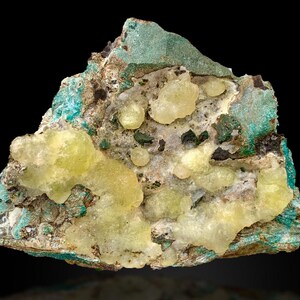 May include: A close-up of a mineral specimen featuring a mix of colors and textures. The base is a mottled mix of brown and gray, with patches of vibrant turquoise and green. Clusters of pale yellow, rounded formations are scattered across the surface.