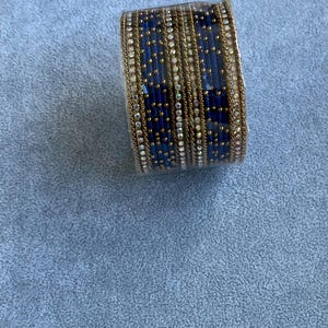 May include: An ornate bracelet with a navy blue and gold design. The bracelet is covered in small, sparkling rhinestones and gold-coloured metal. The bracelet is likely made of metal and glass.