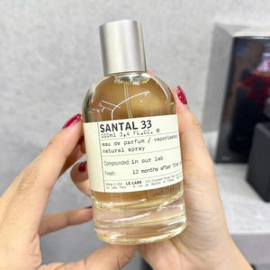 May include: A clear glass perfume bottle with a silver cap, labelled "SANTAL 33". The bottle contains a light amber liquid and is labelled "100ml 3.4 FL.OZ. e eau de parfum / vaporisateur natural spray". The label also states "Compounded: in our lab".