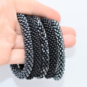 May include: A stack of black and silver beaded bracelets. The bracelets are made of small, round beads and are arranged in a circular pattern.