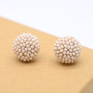 Op de afbeelding: Een paar witte parel oorbelletjes. Elke oorbel is een bol gemaakt van kleine witte parels.