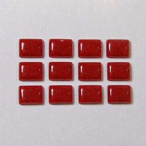 Op de afbeelding: Twaalf rechthoekige cabochons in een levendige rode kleur, gerangschikt in een raster van drie rijen en vier kolommen. Elk stuk heeft een glad, gepolijst oppervlak met afgeronde randen en een consistente, effen rode kleur.